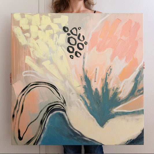 An abstract canvas painting with expressive brushstrokes in peach, cream, teal, and black, held up by a person whose lower body is visible behind it against a plain light wall.